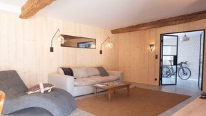 Un salon moderne avec un canapé, un fauteuil aux lignes arrondies, un plancher en bois et une porte donnant accès à un espace de rangement pour vélos.