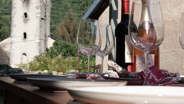 Une table avec des verres à vin et des bouteilles, une table en bois rustique, et une vue sur une tour en arrière-plan.
