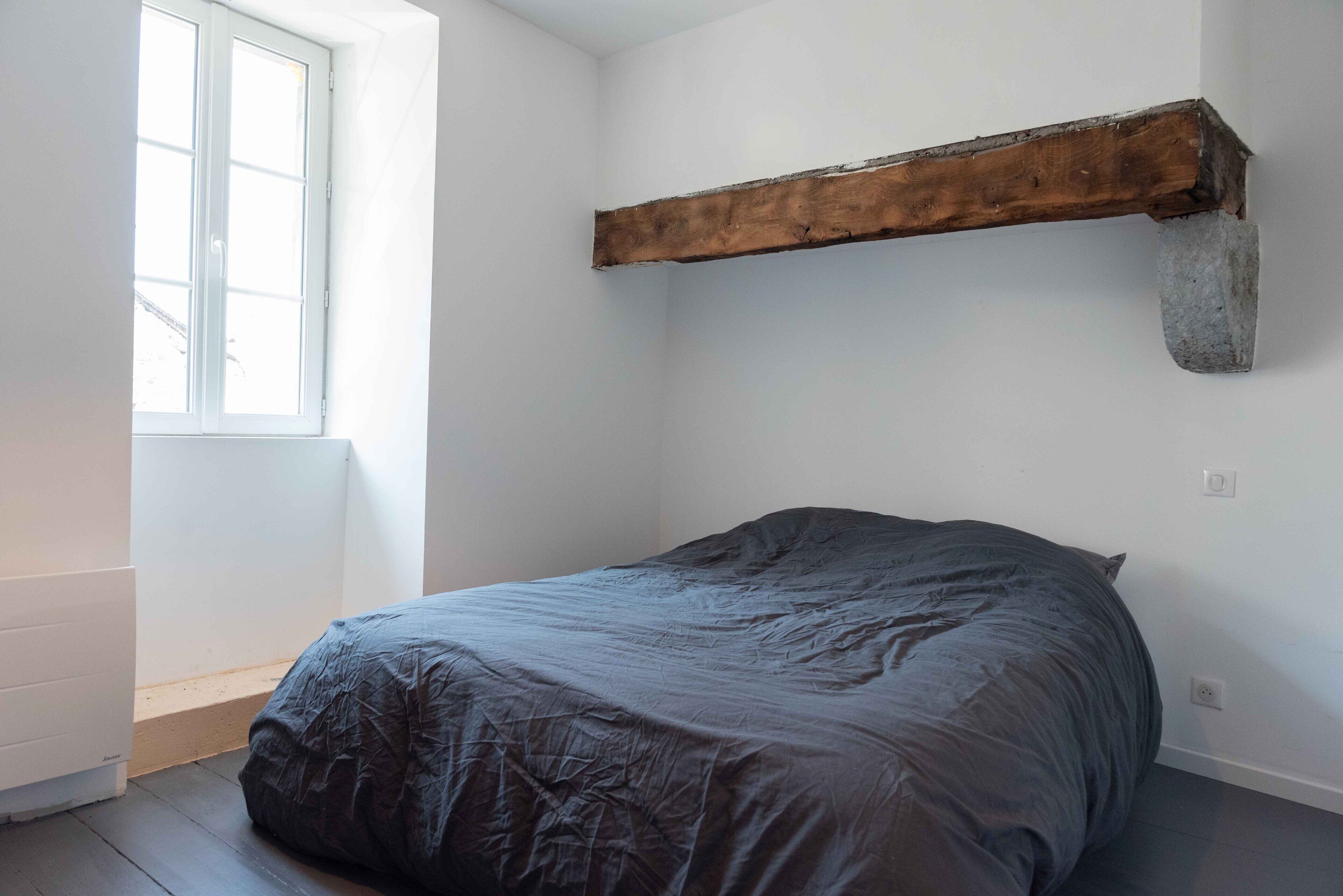 Un dormitorio con una cama, una ventana y una viga de madera en la pared.