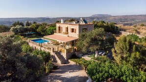Une villa en pierre dotée d’une piscine, entourée d’une végétation luxuriante et adossée à un paysage montagneux.