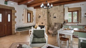 Une pièce chaleureuse avec une cheminée en pierre, un plafond en bois, un coin repas avec une table et des chaises, et un banc.