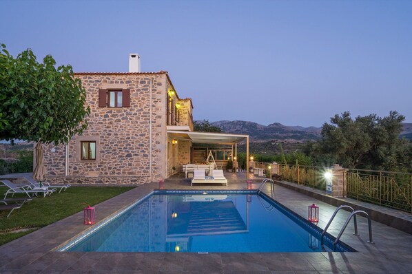 A stone building with a pool, outdoor seating, and a view of mountains.