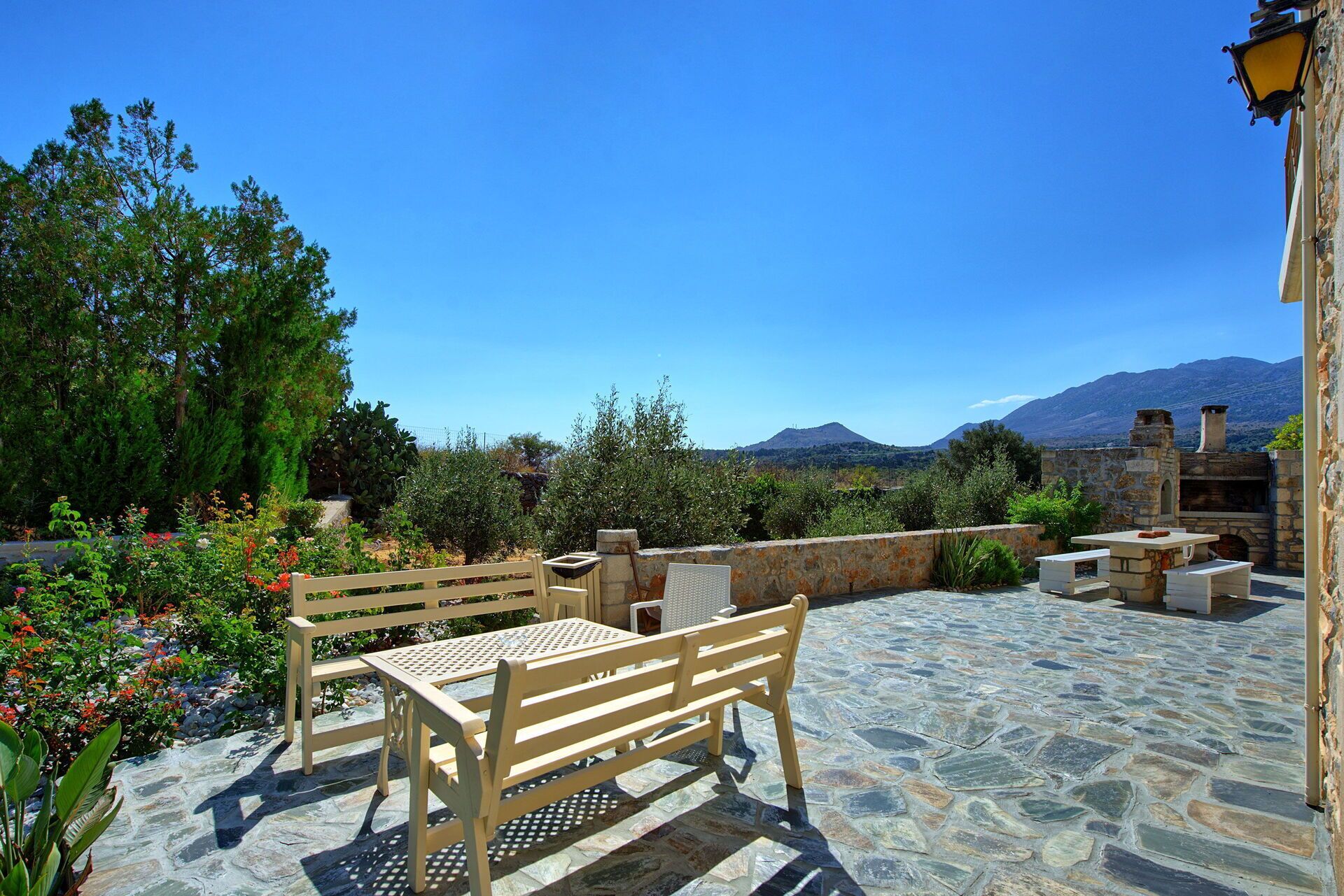 An outdoor patio with stone flooring, a wooden bench, a table, and a stone fireplace.