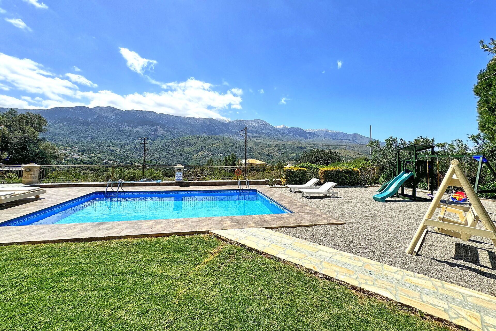 A swimming pool with a mountain view, a slide, and lounge chairs.