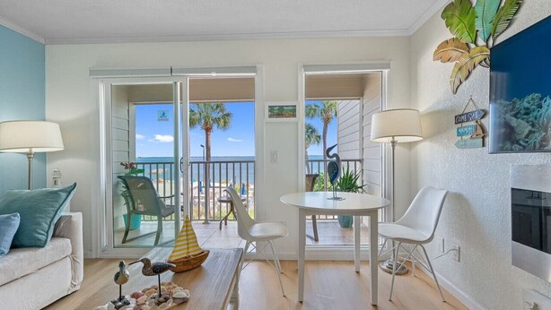 Ein Wohnzimmer mit einer Couch, zwei Sesseln, einem kleinen Tisch und Blick auf den Strand durch Glastüren.