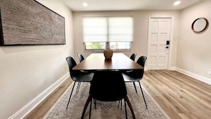 Un comedor con una mesa rectangular, sillas negras, un tapete estampado y un cuadro abstracto grande en la pared.