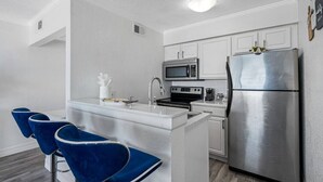A compact kitchen with a central island, bar stools, a stainless steel refrigerator, and a microwave.