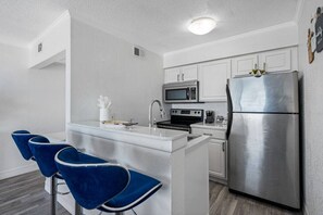 Cocina compacta con una isla central, taburetes de bar, un refrigerador de acero inoxidable y un microondas.