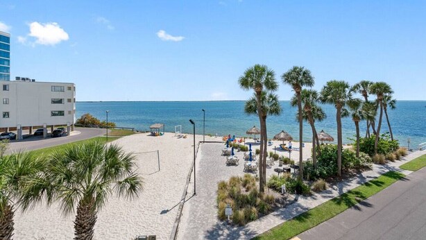 A beach with palm trees, a pool, and a building in the background.