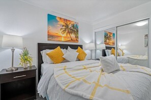 Une chambre d’hôtel avec un lit, des tables de chevet, une lampe, un miroir et un tableau représentant un coucher de soleil.