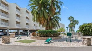 A multi-story building with a parking area, palm trees, and outdoor exercise equipment.