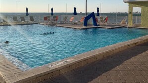 A swimming pool with lounge chairs and umbrellas, a lifeguard stand, and a clear view of the ocean.