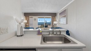 A kitchen with a sink, a window with a view of the sea, and a chair with a towel.