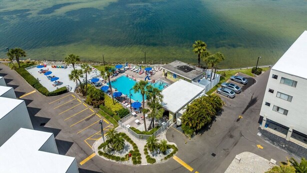 An aerial view of a hotel with a swimming pool, parking area, and a view of the ocean.