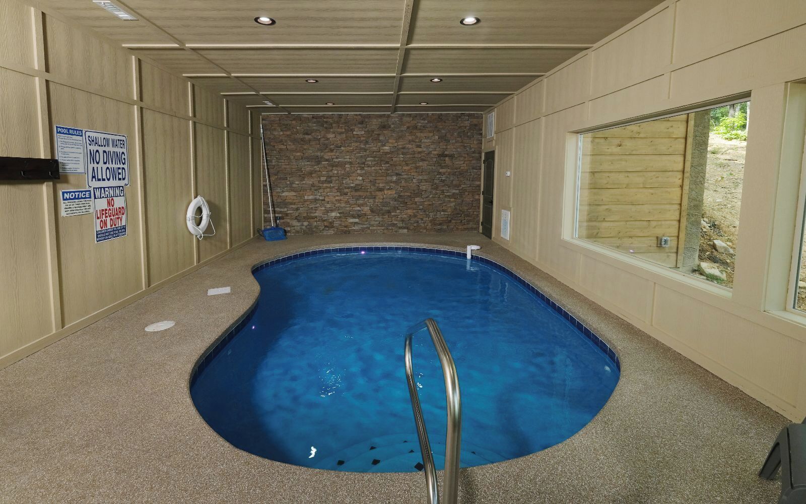 Una piscina interior con un fondo de pared de piedra, una silla de socorrista y carteles con las normas de la piscina.