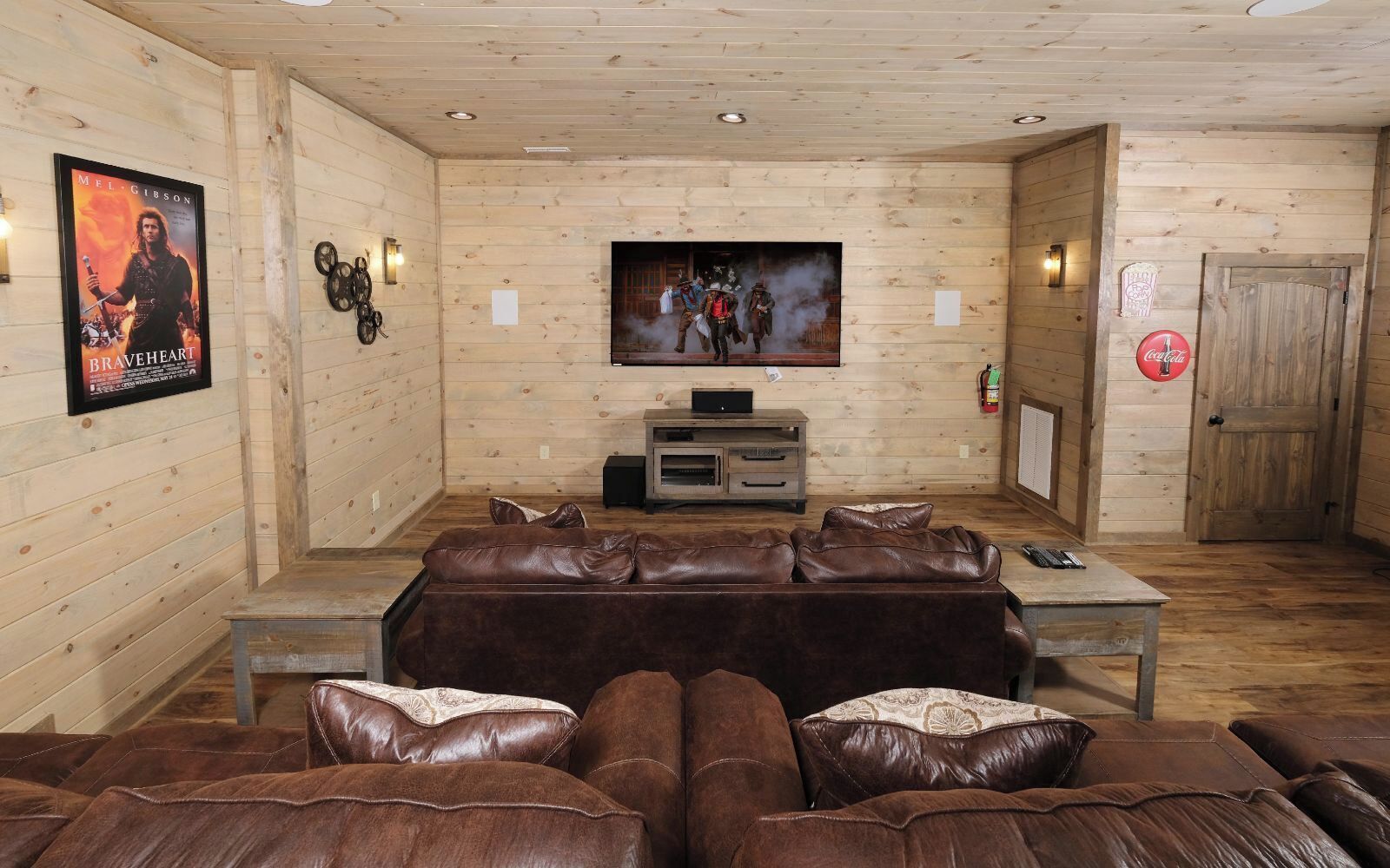 Interior acogedor de una cabaña de troncos con un sofá de cuero, un televisor de pantalla plana y una puerta de madera.