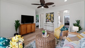 A living room with a television, a ceiling fan, a round woven coffee table, and a sofa with patterned cushions. - PCB Modern Beach Casita, Fully Fenced Yard (Panama City Beach)