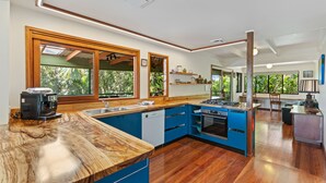 A modern kitchen with blue cabinets, a wooden countertop, and a view of greenery outside. - Farrants Hill (Farrants Hill)