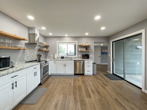 Cocina moderna con armarios blancos, encimera de granito y electrodomésticos de acero inoxidable.