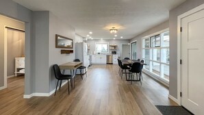 A modern kitchen with white cabinets, a dining area with a wooden table and chairs, and large windows providing natural light. - Excellent location, close to Olympic National Park, restaurants & grocery stores (Port Angeles)