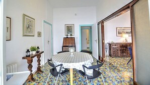 A dining area with a round table, chairs, and a patterned floor. There are framed pictures on the walls and a cabinet in the background.