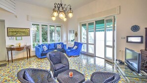 A spacious living area with a large sofa, two armchairs, a glass coffee table, and a television.