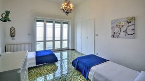 A room with two beds, a chandelier, a window with blinds, and a painting on the wall.