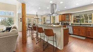 A modern kitchen with a central island, bar stools, wooden cabinets, and a large window.