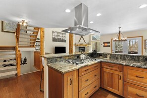 A kitchen with a granite countertop, wooden cabinets, a stainless steel range hood, and a wooden staircase. - 113 Burgundy Circle by Summit County Mountain Retreats (Silverthorne)