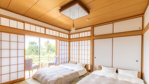 A traditional Japanese-style room with tatami flooring, two beds, a sliding door, and a view of greenery outside. - Resort stay Bowen (Ito)