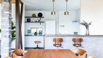 A modern kitchen with a central island, wooden chairs, pendant lights, and a stone pillar.