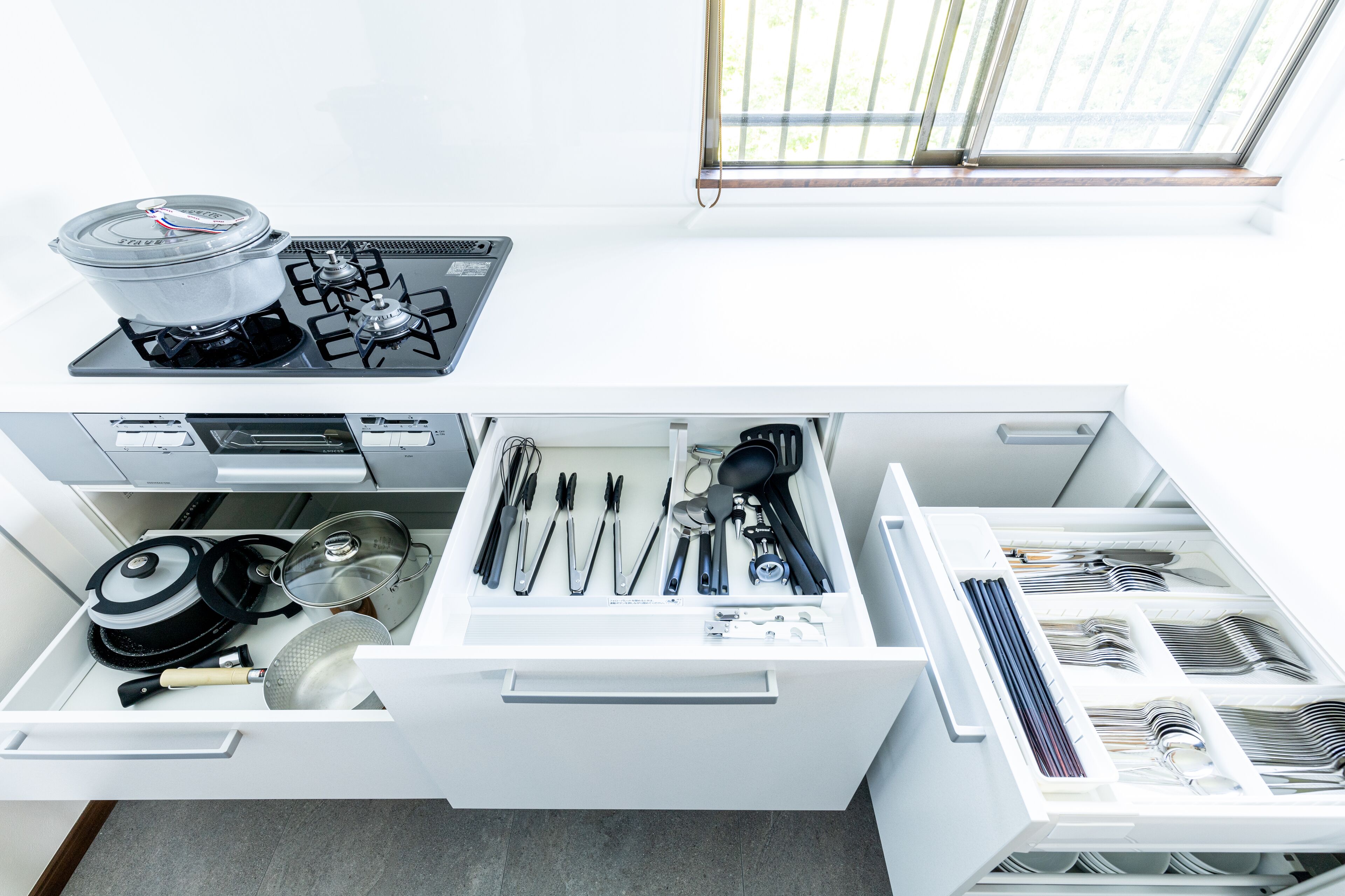 A kitchen with a stove, pots, pans, and utensils neatly organized in drawers.