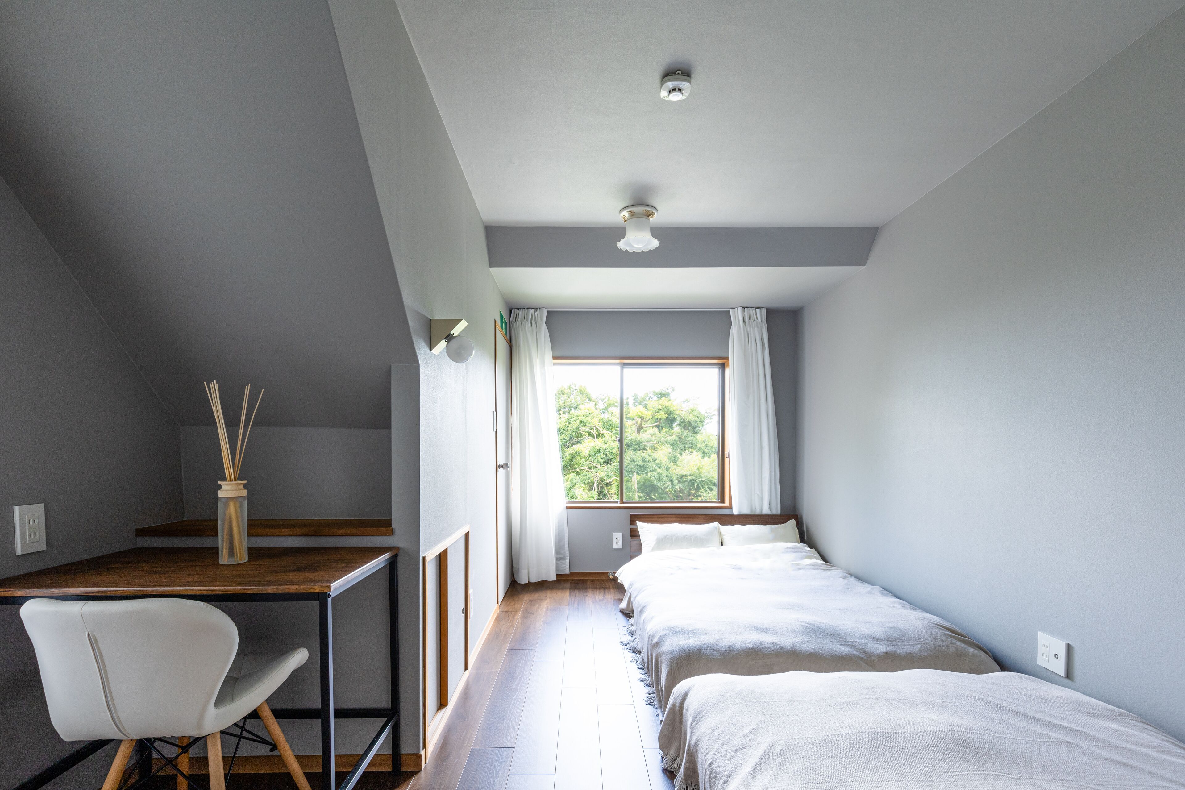 Un dormitorio con escritorio, dos camas, una silla y una ventana con cortinas.