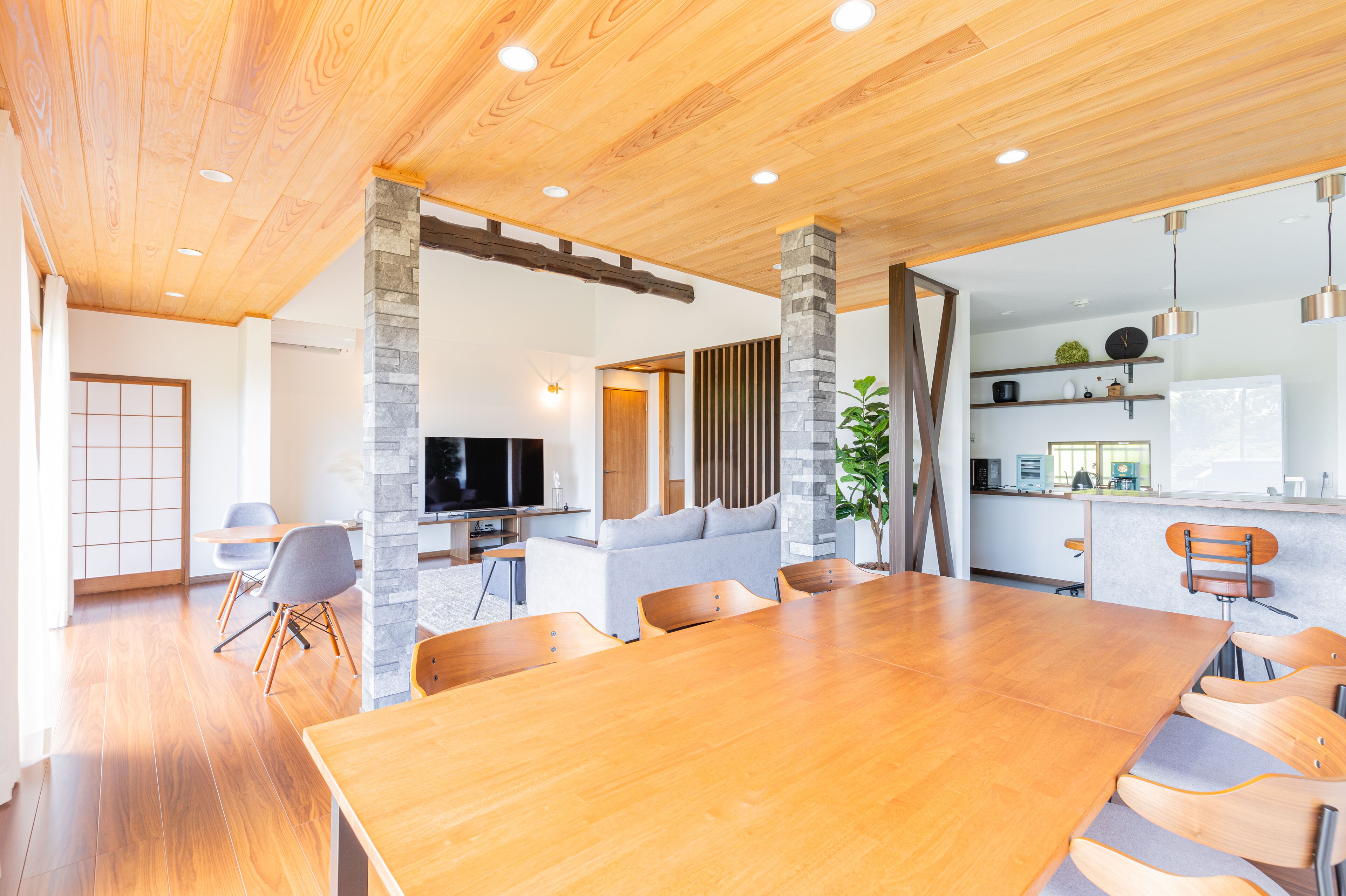 Ein geräumiges Wohnzimmer mit einem Holzesstisch, grauen Sofas und einem Fernseher.