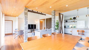 Ein geräumiges Wohnzimmer mit einem Holzesstisch, grauen Sofas und einem Fernseher.