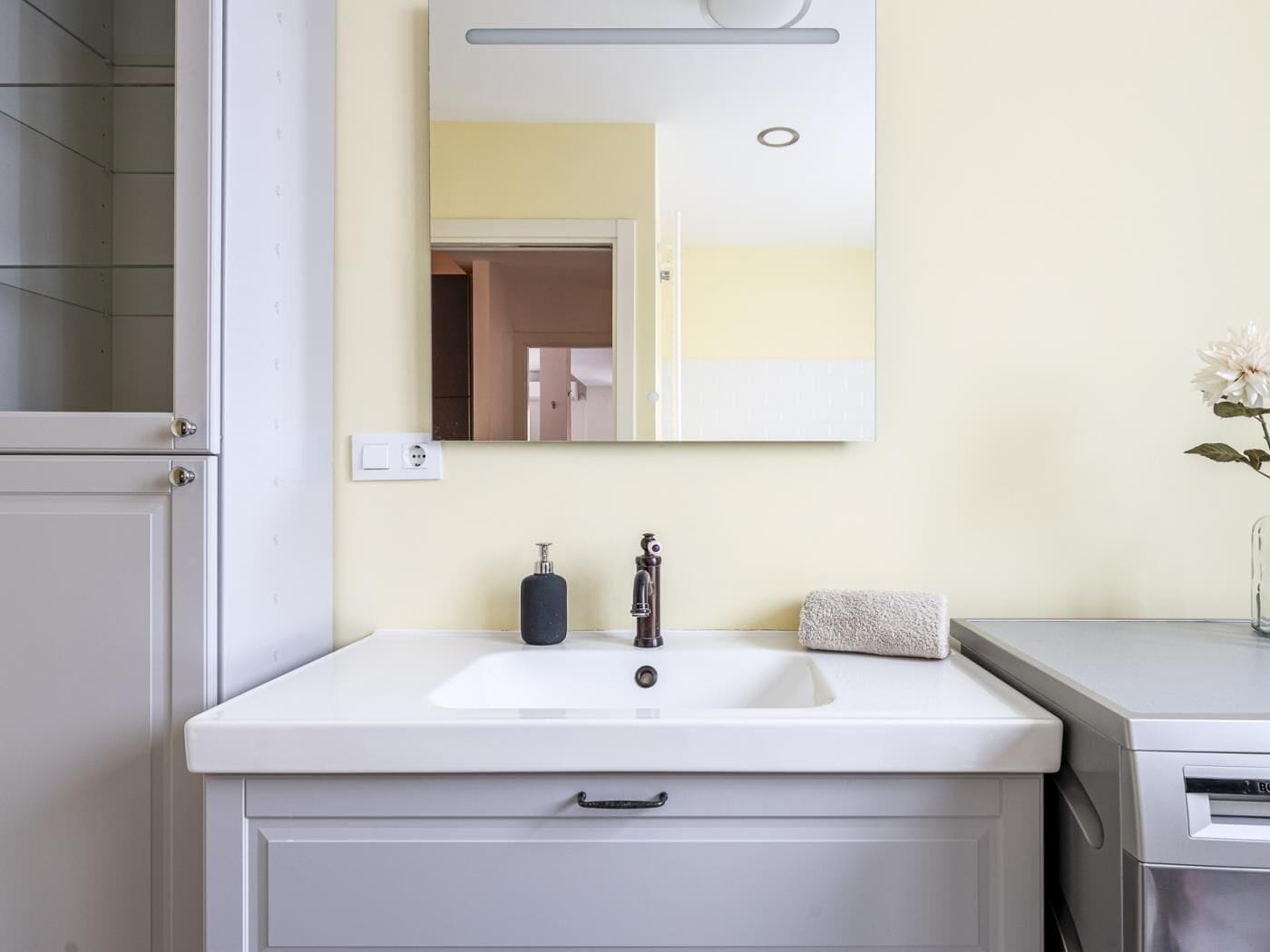 Een badkamer met een wit wastafel, een spiegel, een handdoek en een zeepdispenser.