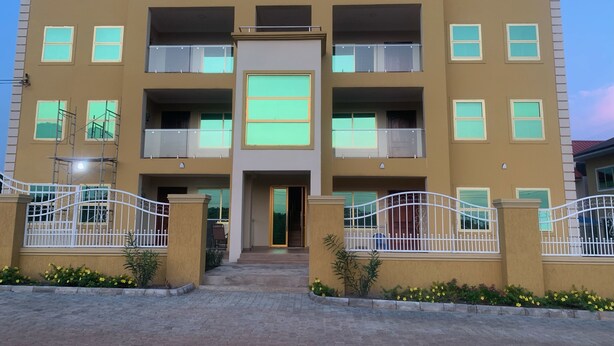 A multi-story building with a central entrance, balconies, and a gated driveway. - Modern and Spacious 2 Bdrm Serviced Apt w/ Patio - Approx. 15 mins from Airport (Accra)