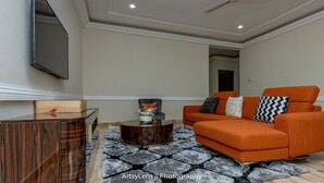 A living room with a modern orange sofa, a wooden coffee table, and a patterned rug. - Modern and Spacious 2 Bdrm Serviced Apt w/ Patio - Approx. 15 mins from Airport (Accra)