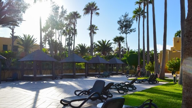 A sunlit outdoor area with lounge chairs and gazebos, surrounded by palm trees and a clear sky. - Casa Bella by Best Holidays Fuerteventura (Corralejo)