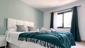 A bedroom with a bed, white headboard, patterned pillows, a teal blanket, and a window with curtains. - Casa Bella by Best Holidays Fuerteventura (Corralejo)
