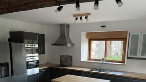 A modern kitchen with a central island, built-in appliances, and a stone accent wall. - Gite de Kerguen (Landaul)