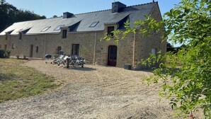 A stone building with a gravel driveway, a barbecue grill, and outdoor seating. - Gite de Kerguen (Landaul)