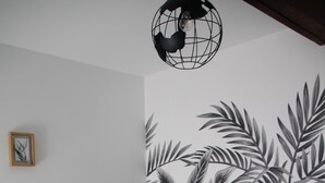 A neatly made bed with a green bedspread and white pillows, a wall with a tropical leaf pattern, and a globe light fixture. - Gite de Kerguen (Landaul)