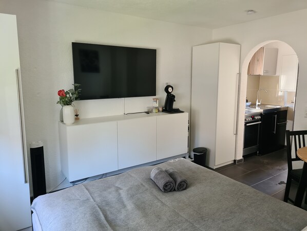 Une chambre d’hôtel moderne équipée d’un lit, d’un téléviseur fixé au mur, d’une petite kitchenette et d’une salle de bain.
