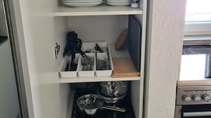 Ett kök med vita hyllor, en spis och diverse köksredskap.