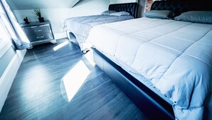Ett modernt sovrum med en inredning i loftstil, med två sängar med grått sänglinne, en byrå och en liten växt placerad på byrån.