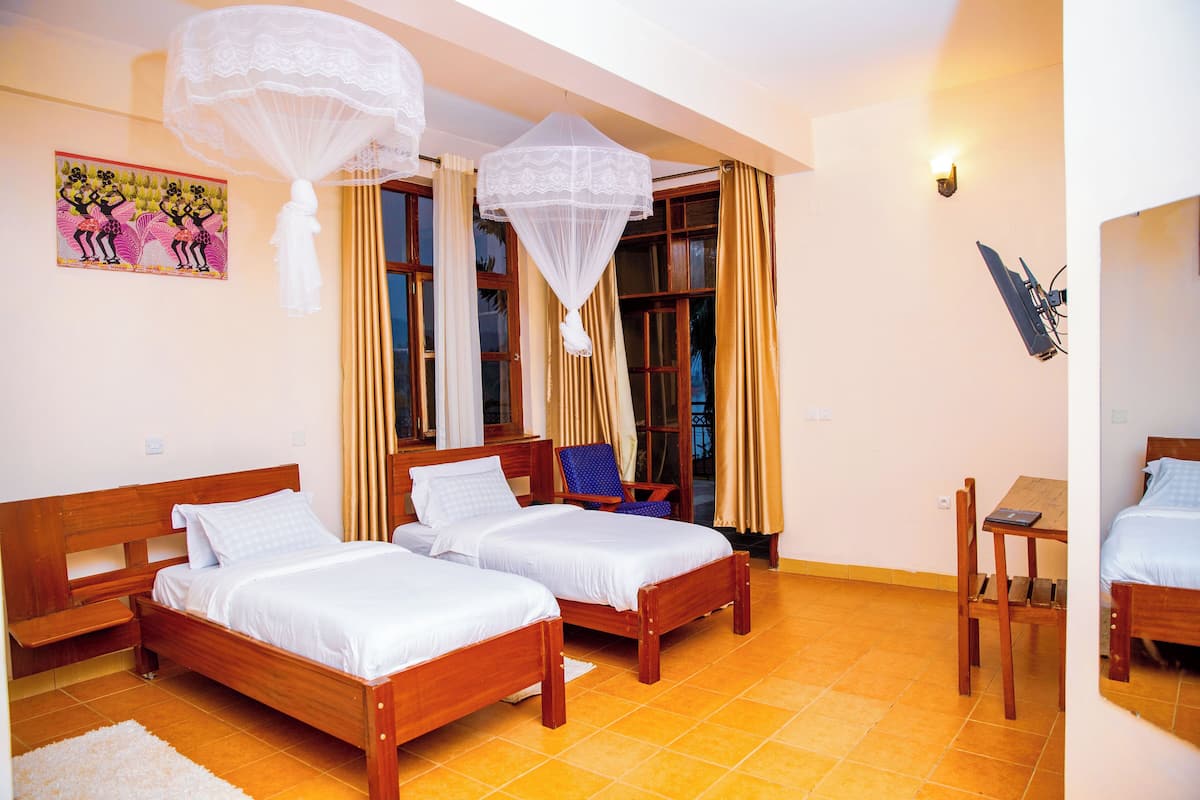 A room with two wooden beds, a chair, a small table, and a wall-mounted TV.
