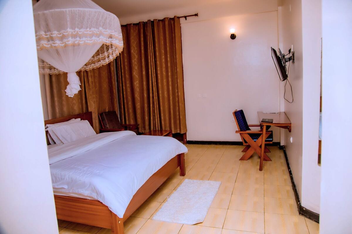 A bedroom with a bed, a desk, a chair, a mosquito net, and curtains.