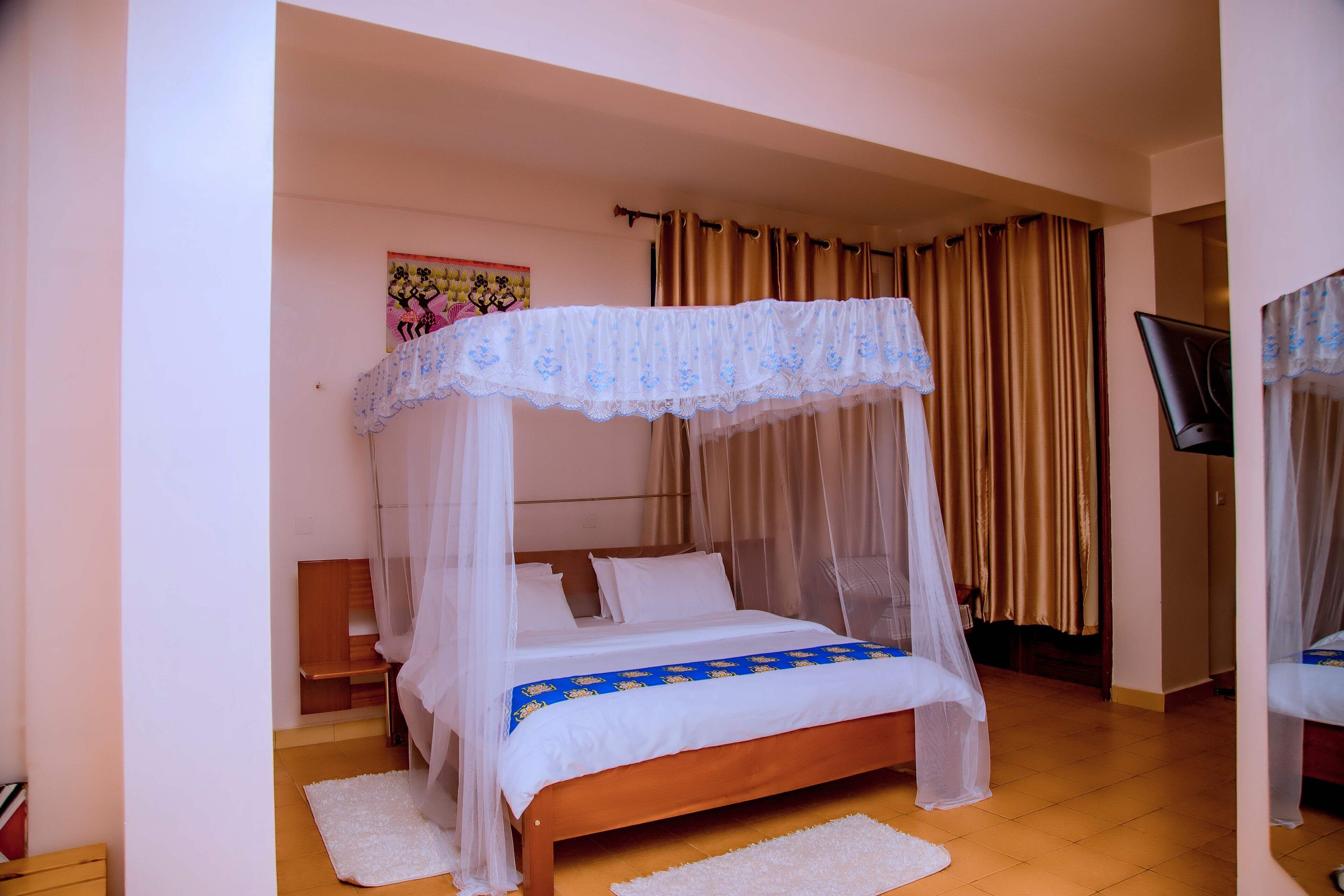 Ein Schlafzimmer mit Himmelbett, einem Holznachttisch, einem weißen Teppich und einem Fernseher auf einem Schrank.