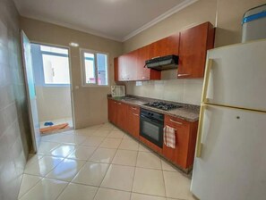 Une cuisine avec des meubles de rangement en bois, une cuisinière, un réfrigérateur et une fenêtre.